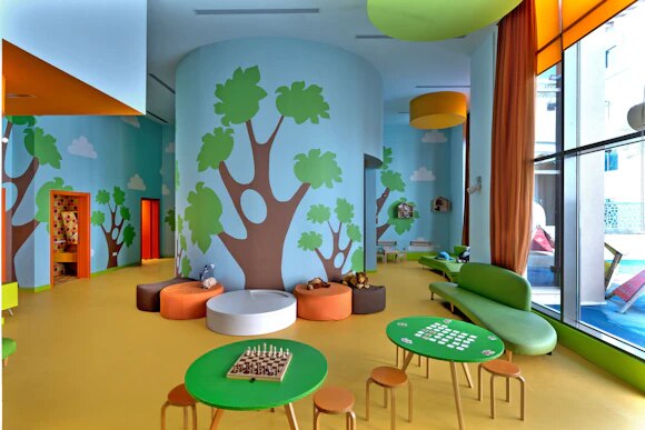 Colourful kids club playroom with painted trees and games tables